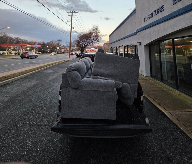 Gray couch on a flatbed trailer outside a storefront at dusk.