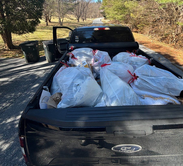 Black Ford pickup loaded with white trash bags on a rural roadside, driver door open