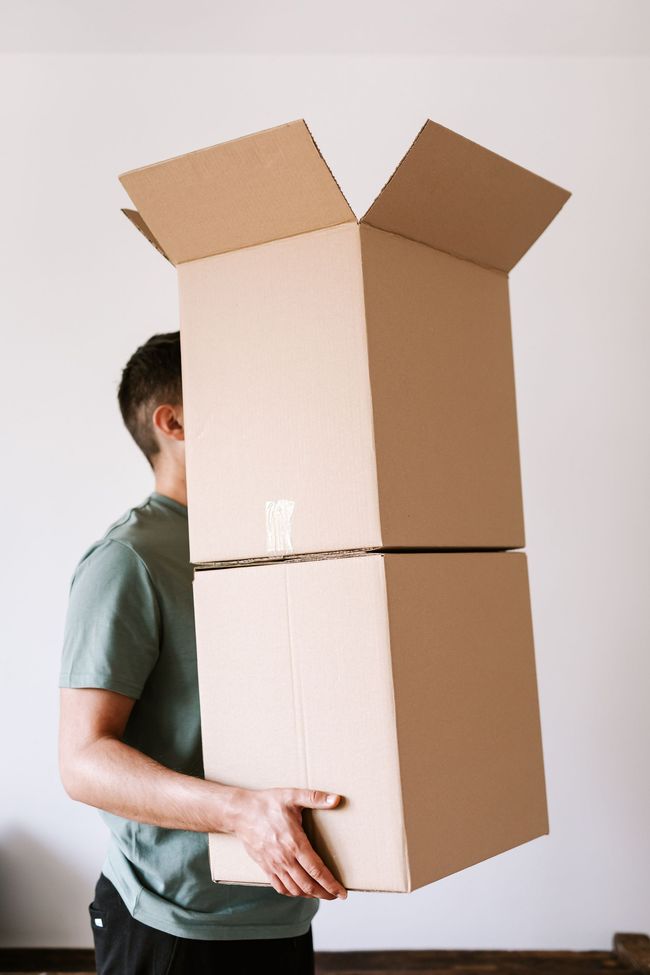Person carrying a tall stack of cardboard boxes with open flaps indoors