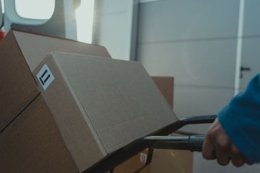 Person using a hand truck to move cardboard boxes in a warehouse