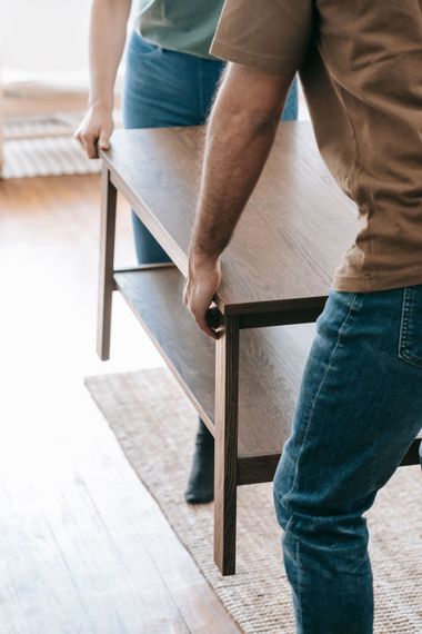 Two people carrying a wooden dining table through a bright room