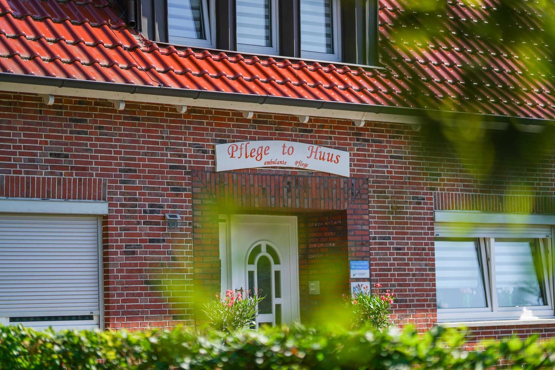 Ein Backsteinhaus mit einem roten Ziegeldach und einem weißen Schild über der Tür. Pflege to Huus. Ambulante Pflege