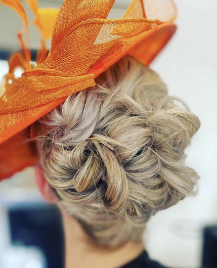 Blonde updo hairstyle with an orange hat or fascinator viewed from the back