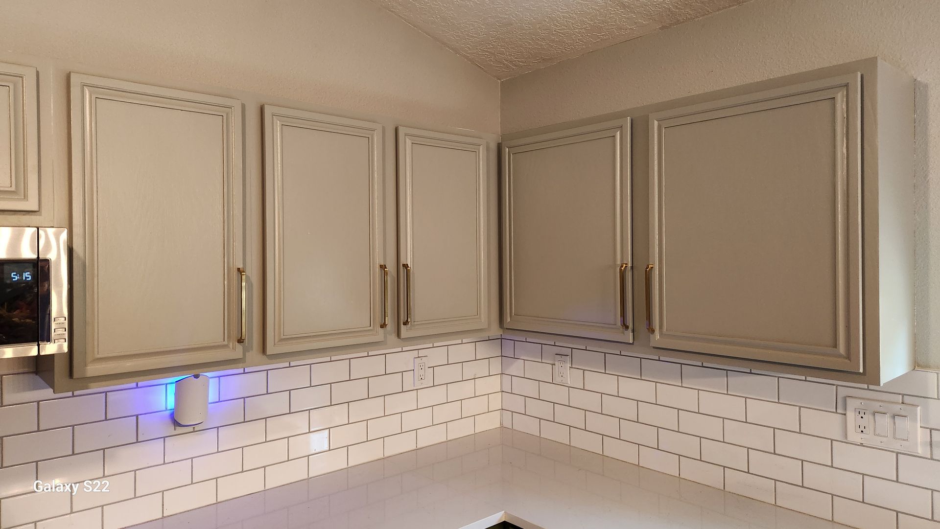 Light gray kitchen cabinets with gold handles over white subway tile backsplash.
