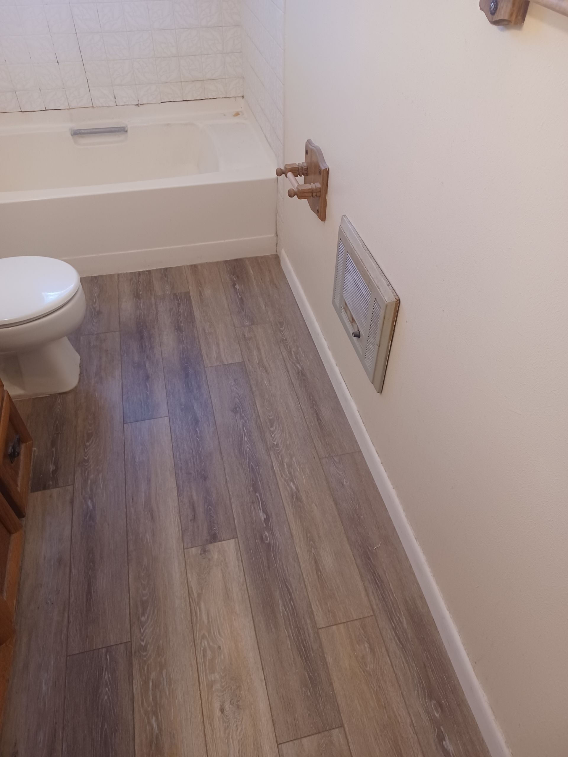 Bathroom with wood-look flooring, a bathtub, toilet, and a wall-mounted heater.