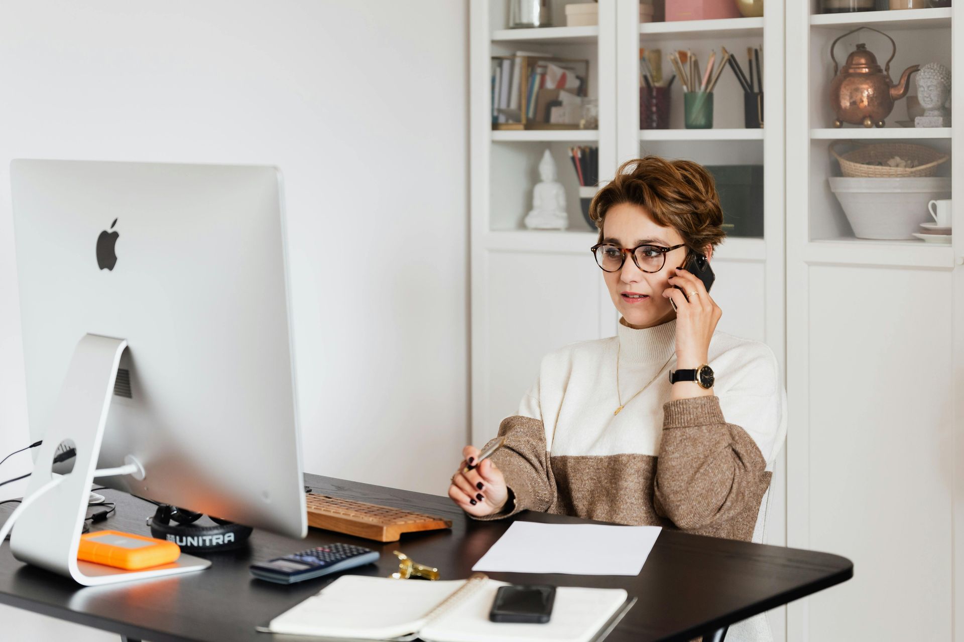 A woman is sitting at a desk talking on a cell phone.