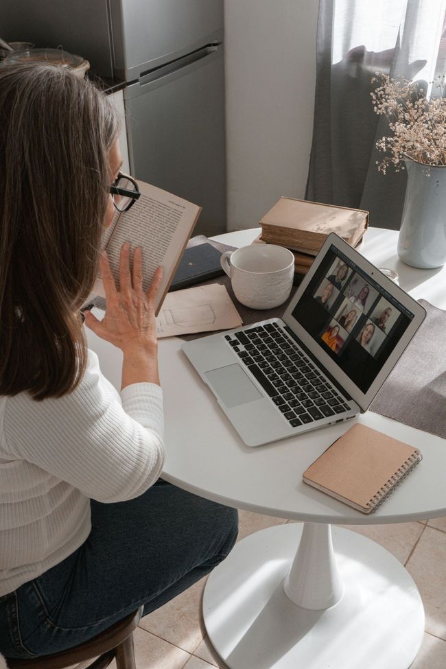 A woman is sitting at a table with a laptop and a book.