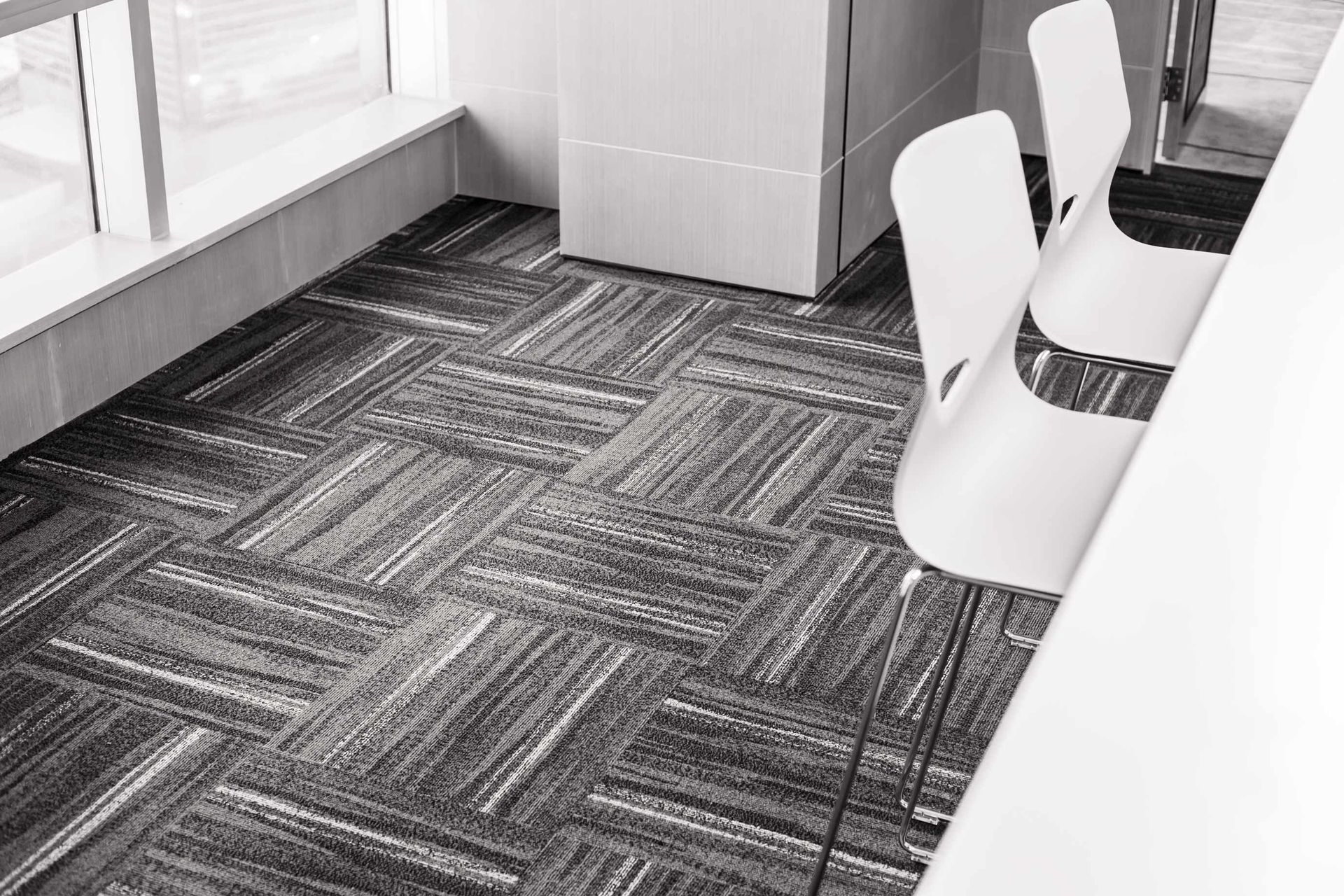 Modern office or meeting room with patterned carpet, white chairs, and large windows.
