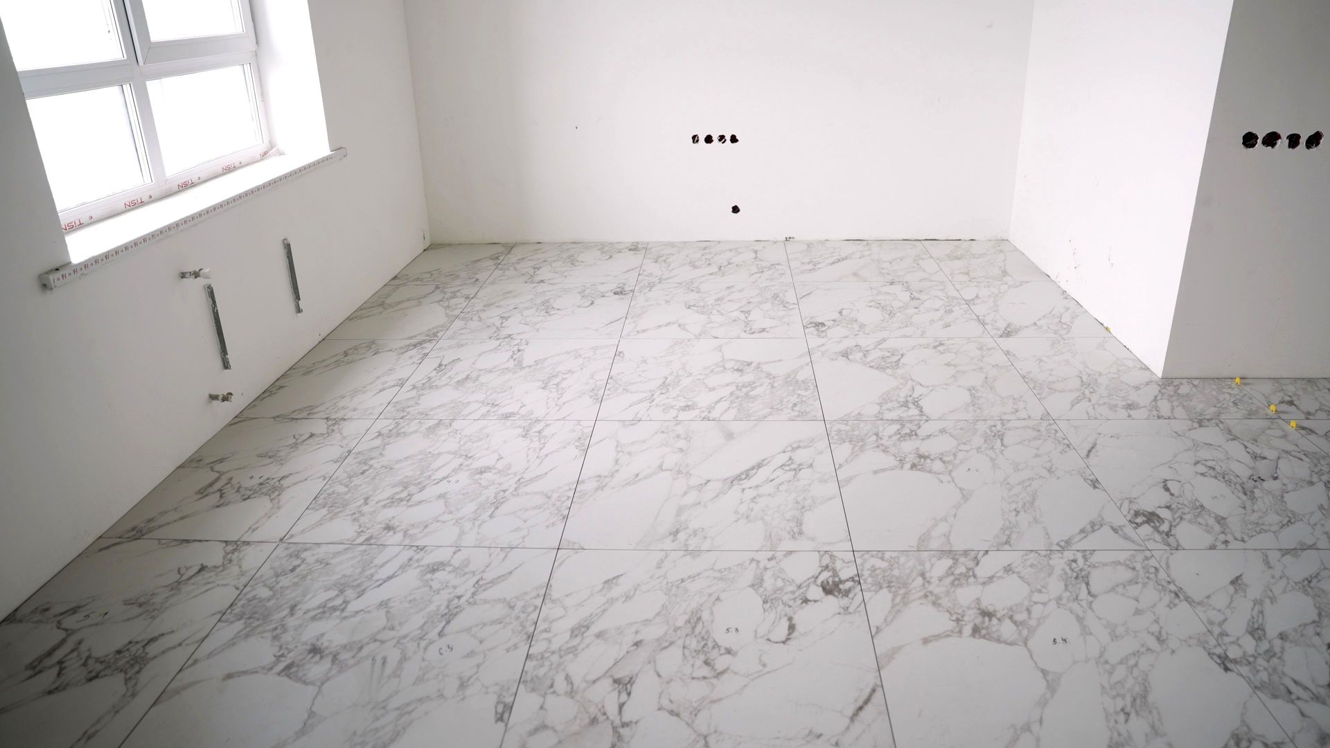 Empty room with white marble floor, plain white walls, and a window on the left.