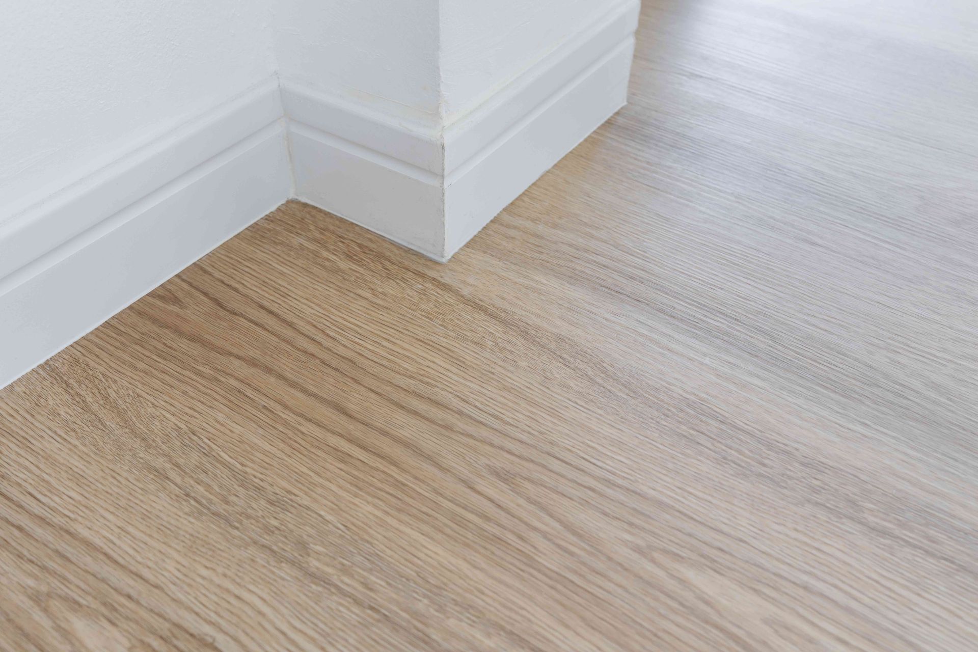 Light wood flooring meeting white baseboards at an interior corner.