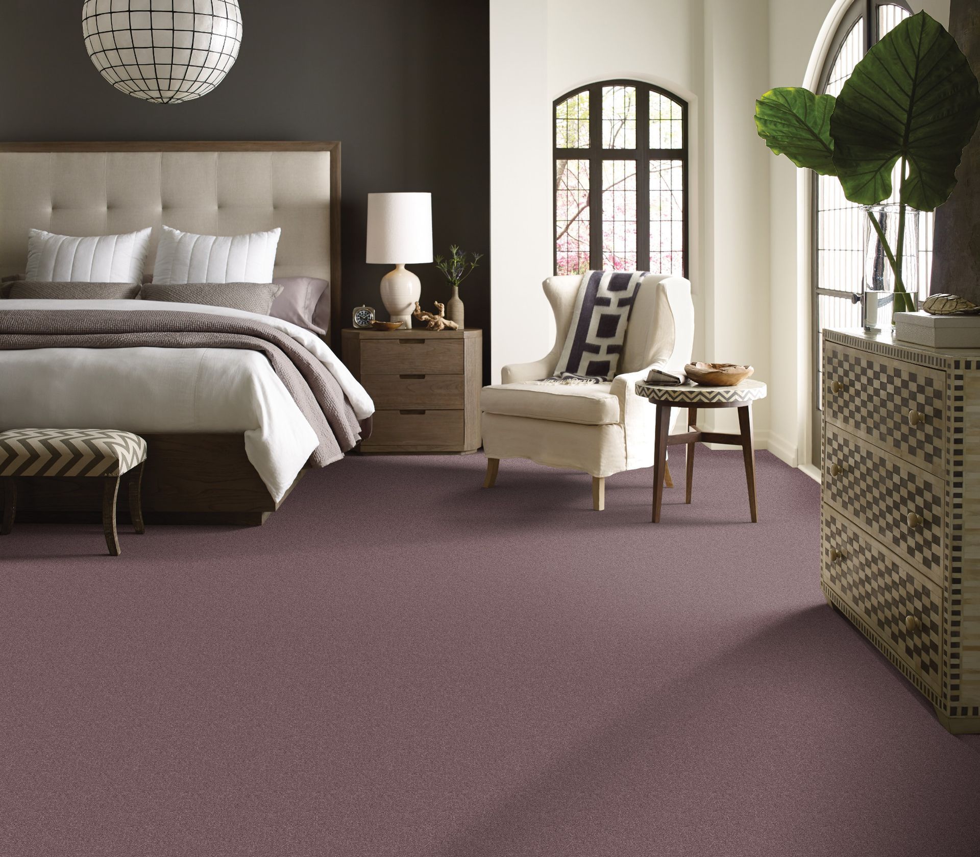 Elegant bedroom with mauve carpet, beige bed, wicker chair, and large window with patterned radiator cover