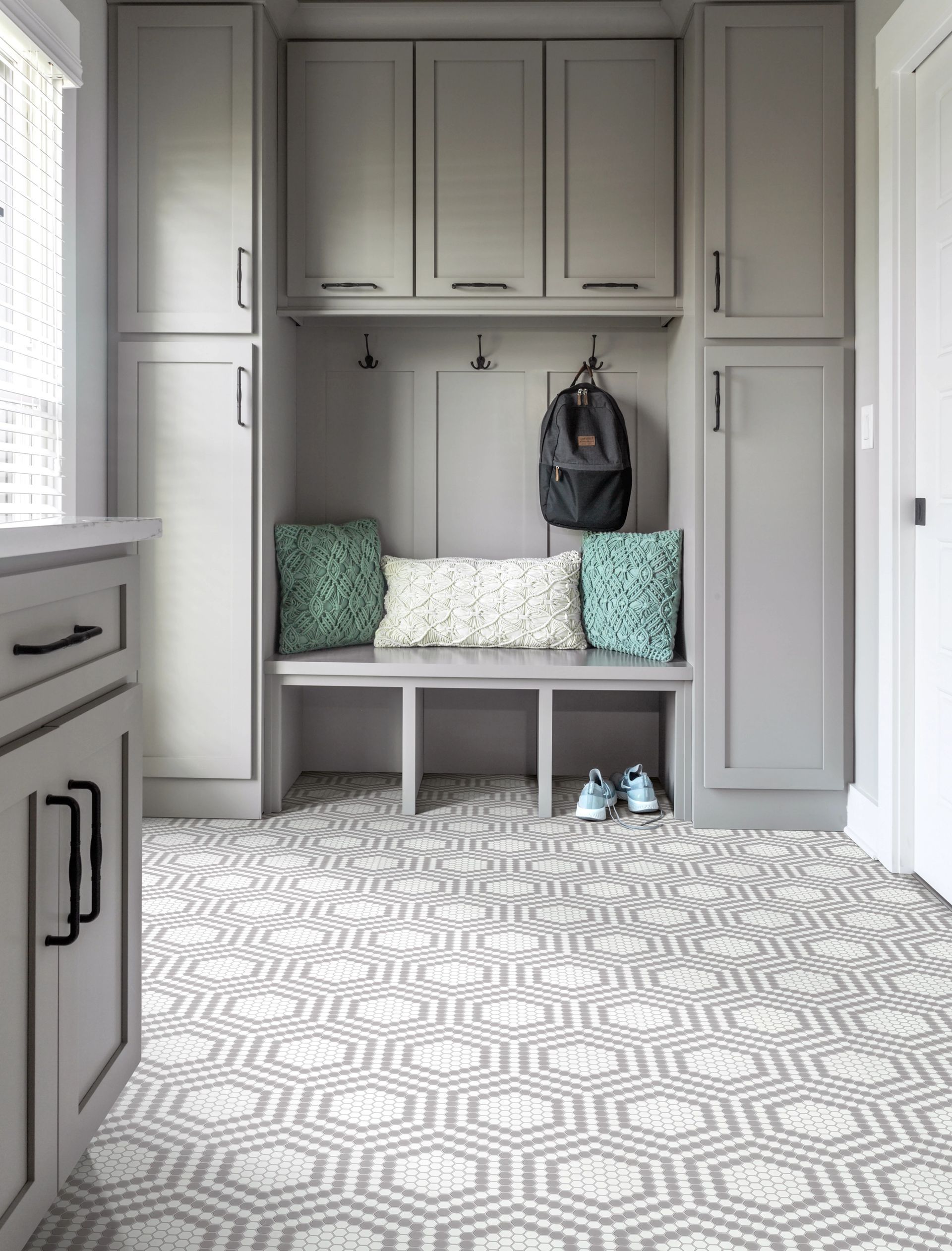 Built-in gray mudroom bench with cubbies, hooks, and patterned floor tile by a doorway.