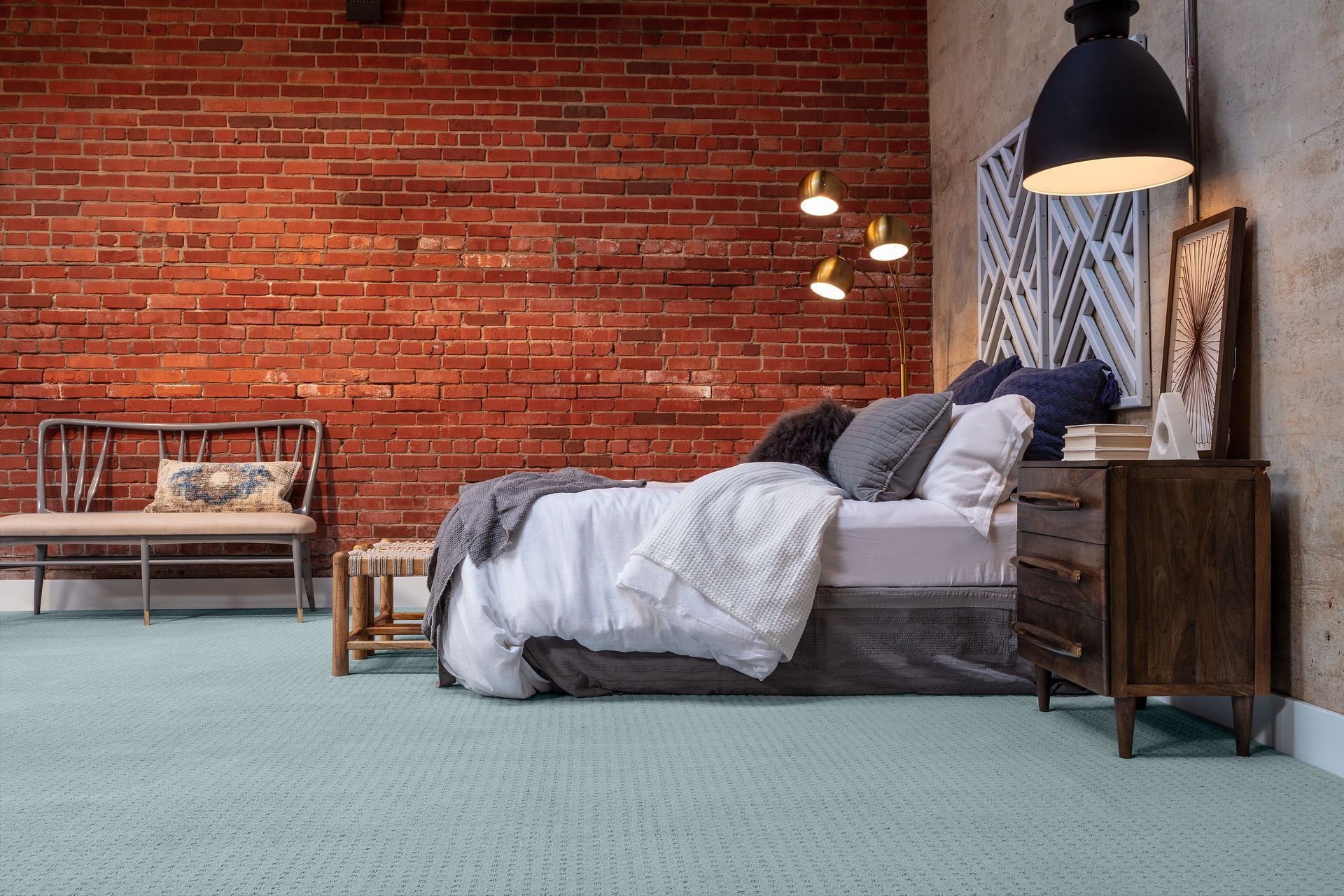 Bedroom with brick wall, gray bed, blue rug, bench, and pendant lamp in a modern rustic style