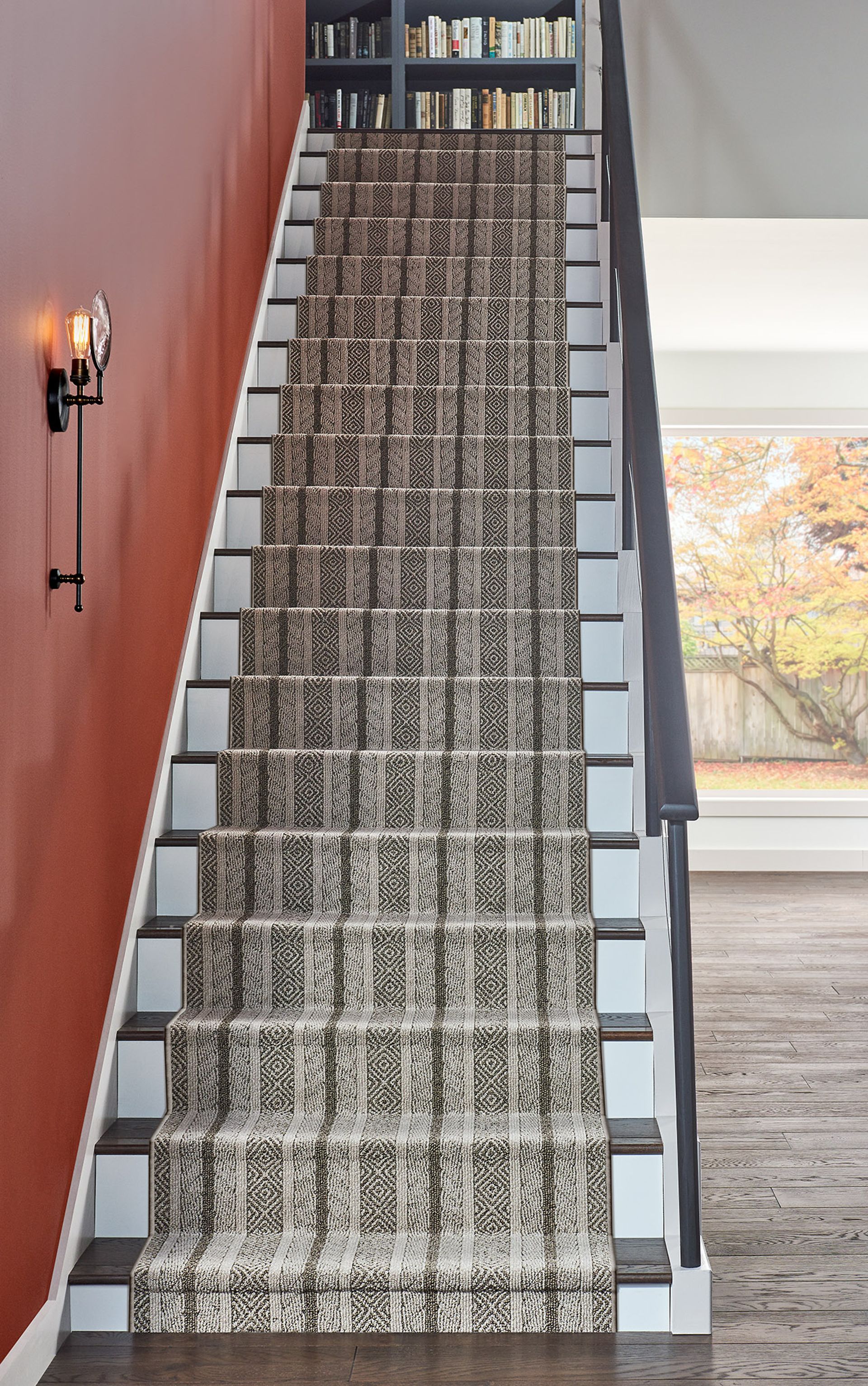 Carpeted staircase with patterned runner in a home, flanked by a red wall and white railing.