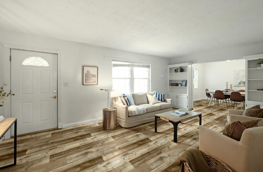 Bright living room with white sofa, coffee table, wall art, and wood flooring, viewed into a dining area