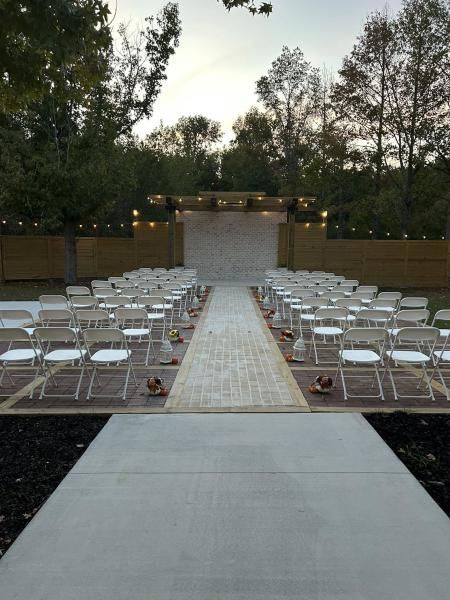 Outdoor wedding ceremony setup with white chairs lining a central aisle in a garden at dusk