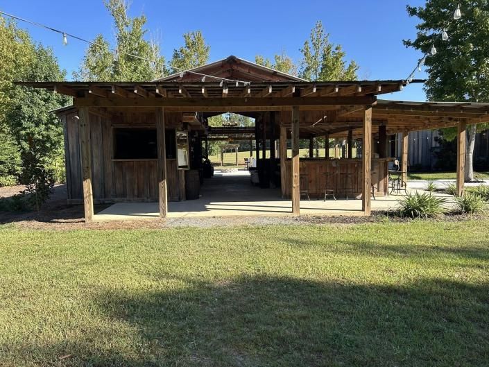 Rustic wooden shed with open front and covered porch in a grassy yard under a clear blue sky