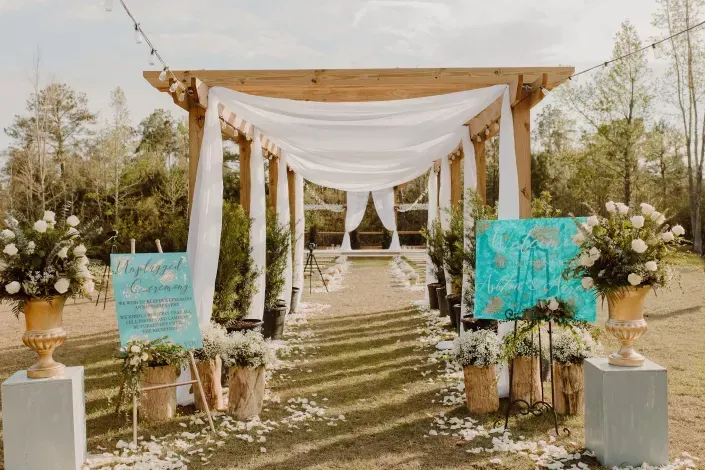 Decorated outdoor wedding aisle with white drapes, floral arrangements, and turquoise signs
