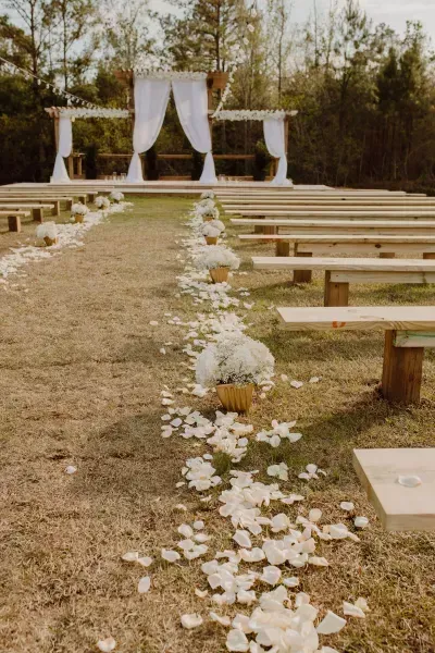 Outdoor wedding aisle with white floral petals leading to a decorated altar and benches on grass