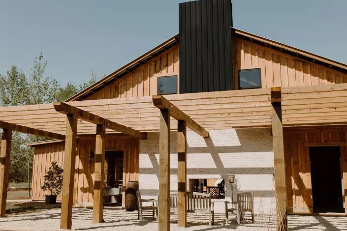 Wooden cabin with a shaded porch and patio chairs under a bright blue sky