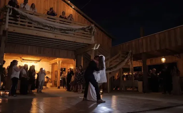 Couple dancing under warm lights in an outdoor plaza at night, with people gathered nearby.