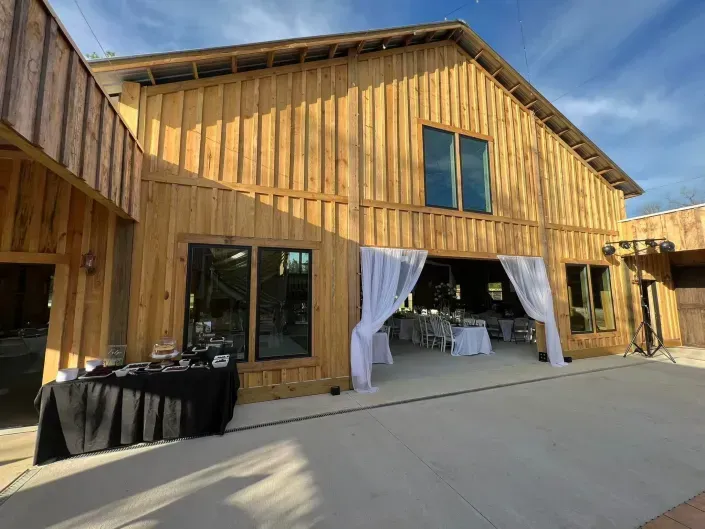 Wooden barn-style event venue with open curtains and tables set up on a concrete patio