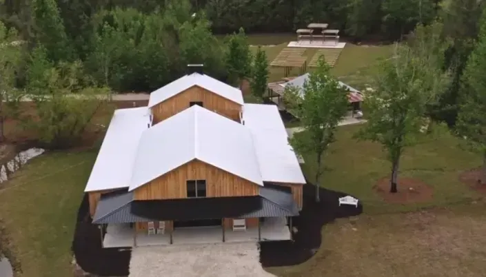 Aerial view of a white-roofed wooden house surrounded by trees and a grassy yard