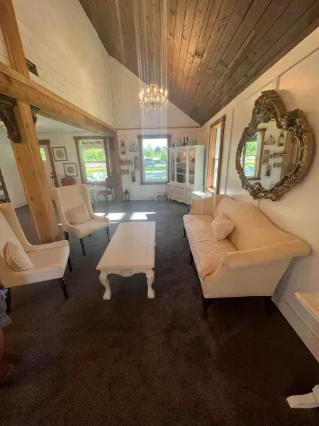 Cozy living room with white sofa, armchairs, coffee table, dark carpet, vaulted wood ceiling, and ornate wall mirror