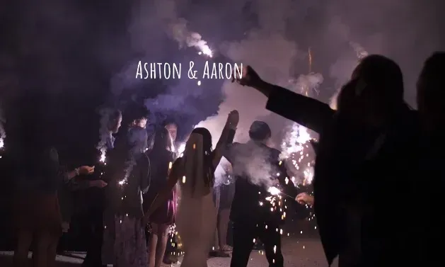 Crowd dancing at a nighttime concert with bright stage lights and “Ashton & Ahu” text above