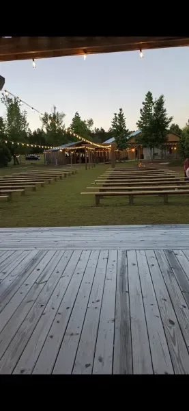 Wooden deck overlooking a grassy amphitheater with string lights and trees at dusk