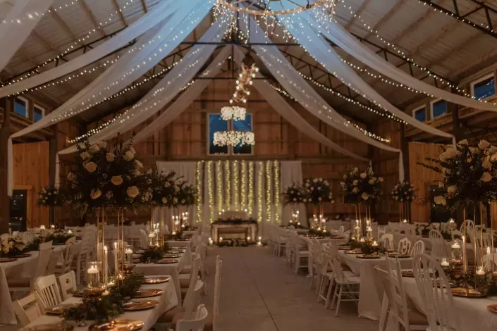 Elegant barn wedding reception with draped lights, chandeliers, and long candlelit tables