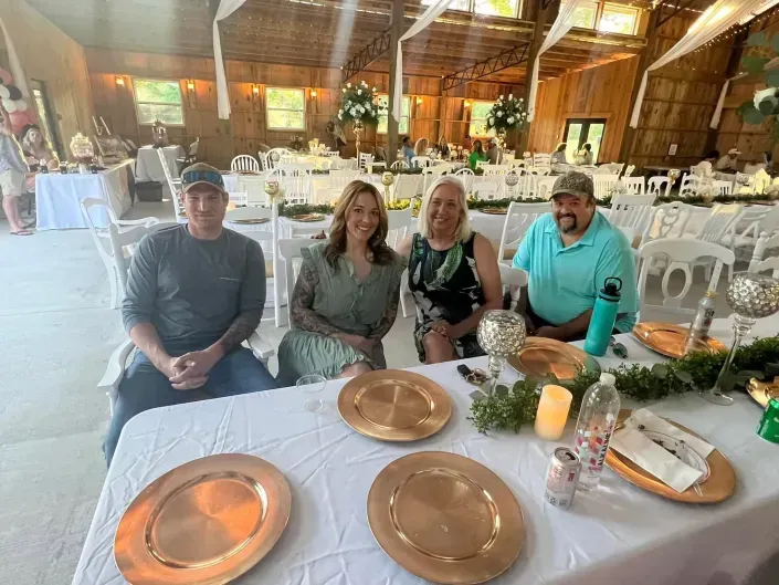 Four people seated at a banquet table in a rustic event hall, smiling toward the camera.