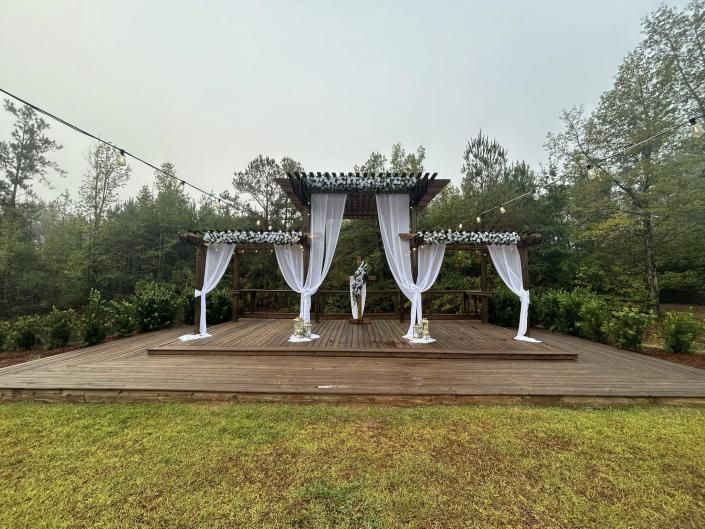 Outdoor wooden wedding arch with white drapes and floral accents on a deck in a green garden
