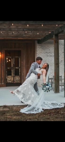 Bride and groom kissing outdoors in front of a rustic venue, bride in white gown holding bouquet