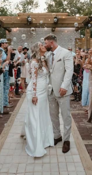 Bride and groom walking down an outdoor aisle under string lights, surrounded by guests.
