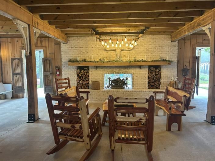 Rustic living room with wooden chairs facing a stone fireplace and chandelier under exposed beams