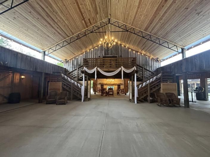 Rustic barn interior with a high wooden ceiling, central draped stage, and wide open concrete floor