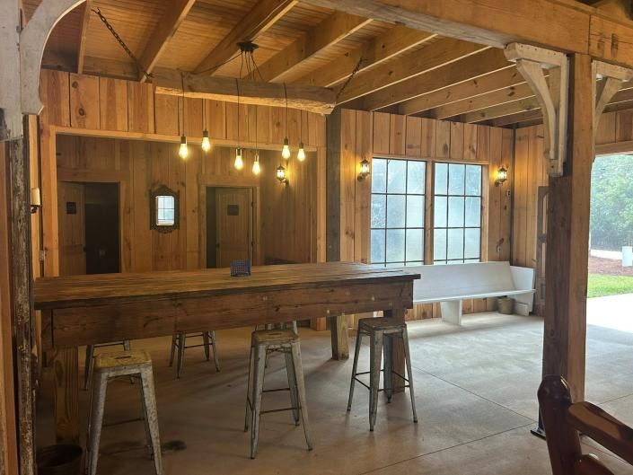Rustic wooden bar interior with stools, pendant lights, and large windows overlooking a porch