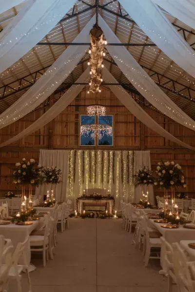 Elegant barn wedding reception with white drapery, string lights, and candlelit tables