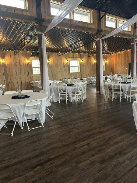 Empty banquet hall with white round tables and chairs, dark wood floor, and warm string lights on bamboo walls