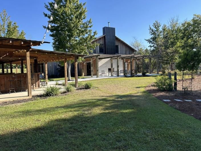 Grassy courtyard with wooden pergolas, trees, and a rustic building under a blue sky.