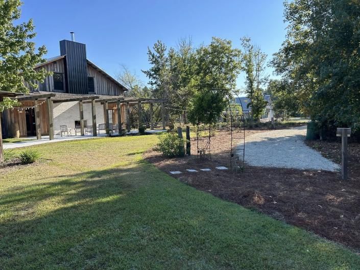 Grassy yard beside a rustic house with trees and a gravel path under a clear blue sky