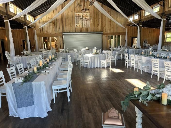 Rustic barn wedding reception with white chairs, round tables, and draped fabric ceiling décor