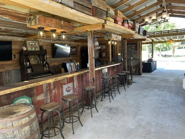 Rustic outdoor bar with wooden stools, barrel decor, and a covered patio walkway