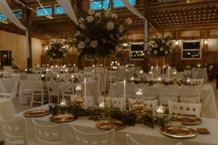 Elegant banquet hall set for a wedding reception with white chairs, candlelit tables, and floral centerpieces