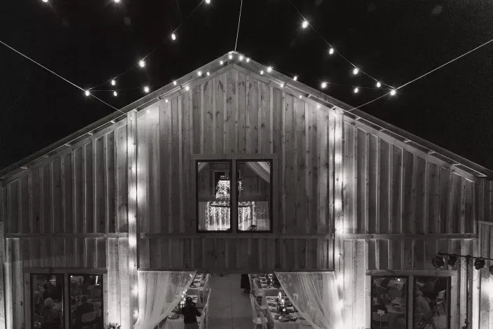 Black-and-white barn lit with string lights, with a figure visible in the upper window.