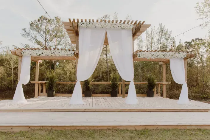 Outdoor wedding altar with white drapes and wooden canopy on a raised platform