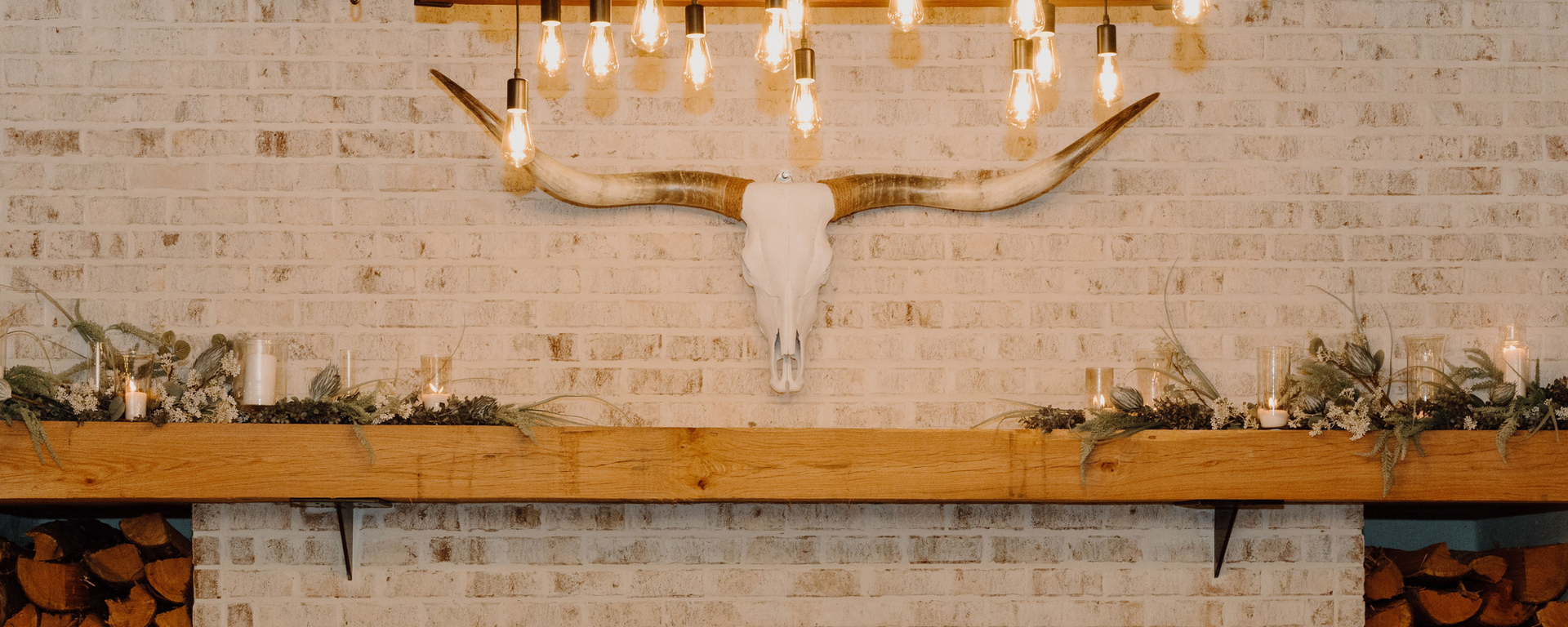 Rustic indoor shelf with candles, greenery, and a deer skull wall mount on a white brick wall