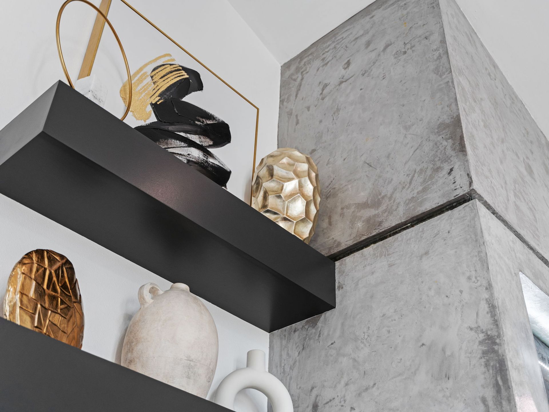 Decorative shelves with gold, black, and white vases against a gray concrete wall