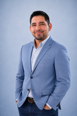 Portrait of a smiling man in a navy blazer and white shirt against a light gray background
